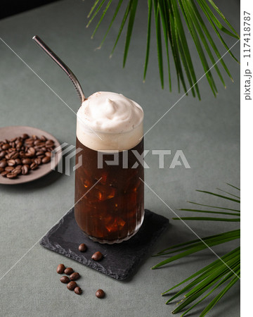 Iced coffee brew with foam in a glass on a black board on a dark green background with coffee beans  117418787