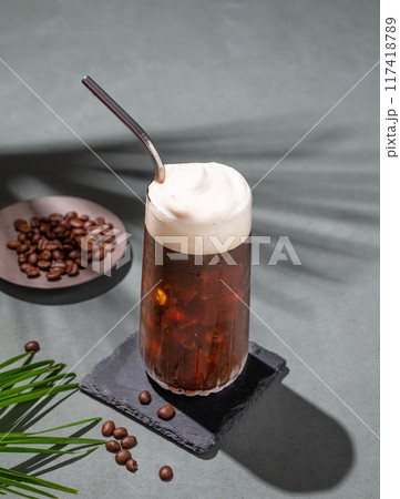 Iced coffee brew with foam in a glass on a black board on a dark green background with coffee beans Iced coffee brew with foam in a glass on a black board on a dark green background with coffee beans 117418789