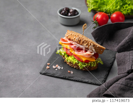 Club sandwich on a board with a bacon, cheese, tomato and lettuce on a dark background Club sandwich on a board with a bacon, cheese, tomato and lettuce on a dark background 117419073