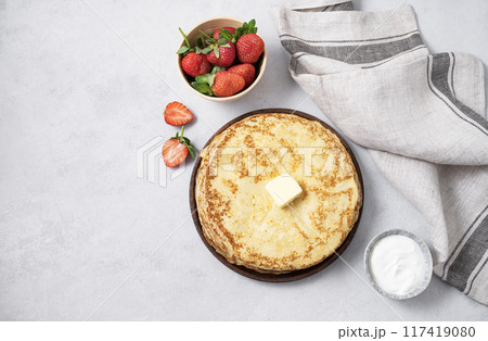 Sweet pancakes stacked with butter, sour cream and fresh strawberries on a light background. 117419080