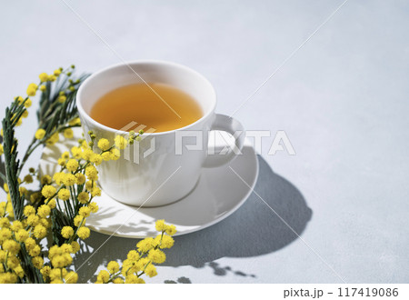 A spring bouquet with yellow mimosa flowers and a cup of herbal tea on a light background A spring bouquet with yellow mimosa flowers and a cup of herbal tea on a light background 117419086