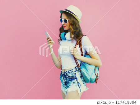 Stylish modern young woman listening to music in headphones with phone on pink background Stylish modern young woman listening to music in headphones with phone on pink background 117419304