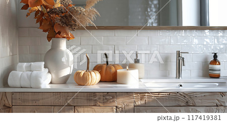 Modern bathroom with white tiles and wooden vanity. Small pumpkins placed on the vanity next to candles and vase of autumn flowers. Minimalist design. 117419381