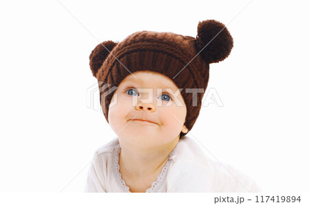 Portrait close up of cute baby wearing a winter knitted brown hat looking up over a white background Portrait close up of cute baby wearing a winter knitted brown hat looking up over a white background 117419894