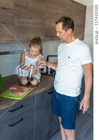 Young father and daughter cooking fish together in home kitchen 117420589