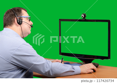 Office Manager with Headset Gazes at Green-Screen Monitor During Virtual Meeting or Telemedicine Consultation, Capturing Modern Remote Work or Healthcare Office Manager with Headset Gazes at Green-Screen Monitor During Virtual Meeting or Telemedicine Consultation, Capturing Modern Remote Work or Healthcare 117420734