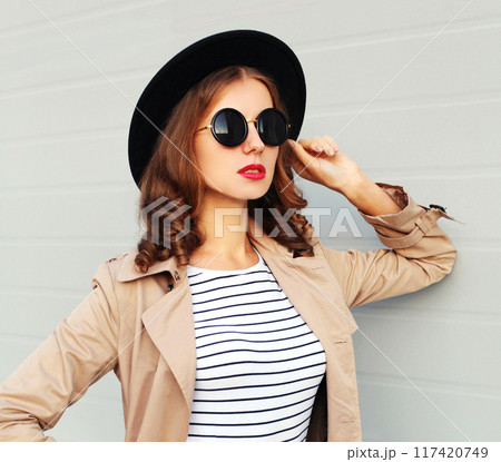 Portrait of stylish young woman posing in black round hat, glasses in the city on gray background Portrait of stylish young woman posing in black round hat, glasses in the city on gray background 117420749