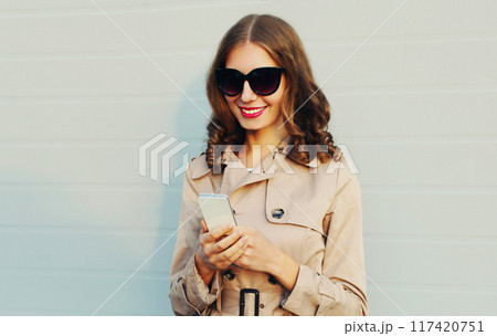 Portrait of stylish happy young woman holding smartphone on gray background Portrait of stylish happy young woman holding smartphone on gray background 117420751