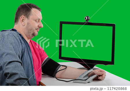 Large Man Seated Next to Green-Screen Monitor Measures Blood Pressure, Showcasing Telehealth Services for Hypertension Monitoring. Large Man Seated Next to Green-Screen Monitor Measures Blood Pressure, Showcasing Telehealth Services for Hypertension Monitoring. 117420868