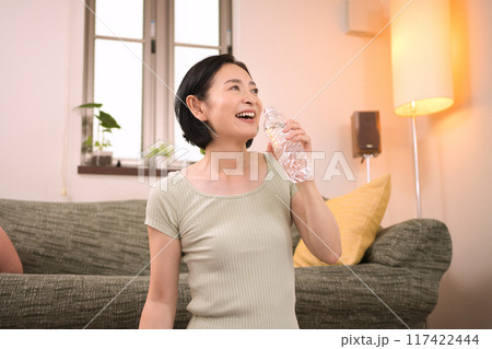 リビングでペットボトルの水を飲むスポーツウエアのミドル女性 117422444
