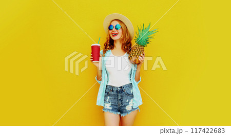 Portrait happy smiling woman holding pineapple, cup of juice in summer on colorful yellow background Portrait happy smiling woman holding pineapple, cup of juice in summer on colorful yellow background 117422683