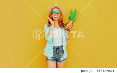 Portrait happy smiling woman with pineapple having fun in summer hat, glasses on yellow background 117422684