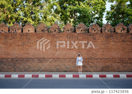 A woman stands in front of a brick wall, looking at her phone A woman stands in front of a brick wall, looking at her phone 117423856