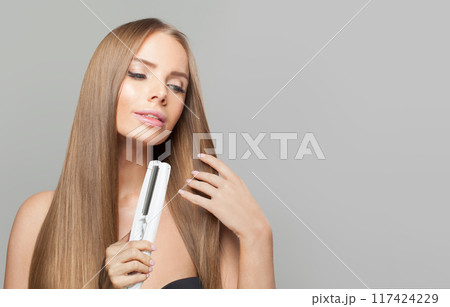 Joyful brunette lady with straight hair holding straightening iron  117424229