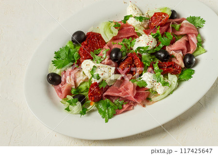 salad with dried tomatoes, prosciutto, soft cheese, olives, homemade, top view, 117425647