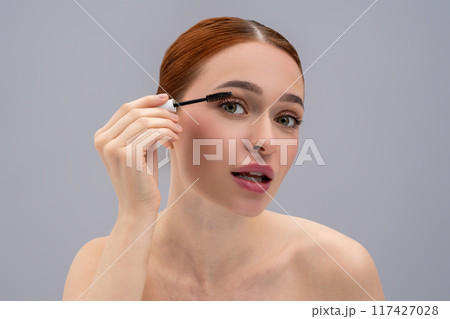 Pretty red-haired girl using brush to apply mascara 117427028