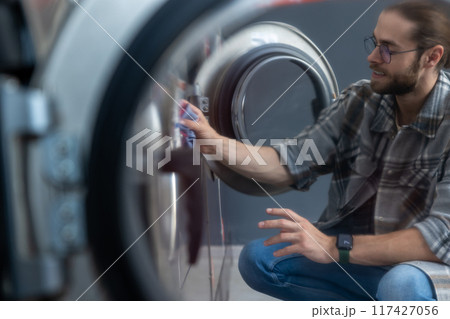 Hard working bearded man washing clothes at self-service laundromat Hard working bearded man washing clothes at self-service laundromat 117427056