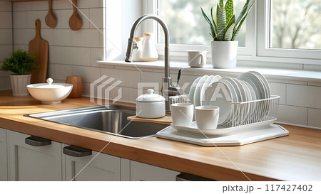 Dish rack holds many dishes and cups against wooden countertop, white wall tiles, sink and faucet. Budget and lightweight antimicrobial dish drainer with drain board at modern scandinavian kitchen 117427402