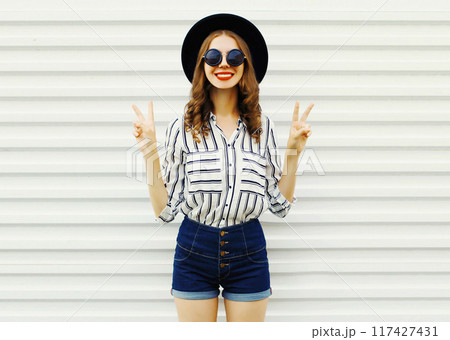 Happy smiling cool girl in black round hat, shorts, white striped shirt posing on white background 117427431