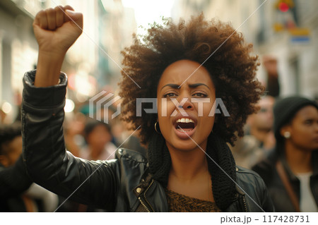 Young woman leads crowd in protest Shouting and raising fists in the street. 117428731
