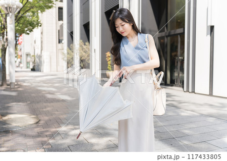 オフィス街の歩道で日傘を差そうとしてるビジネスウーマン 117433805