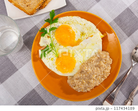Portion of diet food on plate - two fried eggs and boiled oatmeal porridge Portion of diet food on plate - two fried eggs and boiled oatmeal porridge 117434189