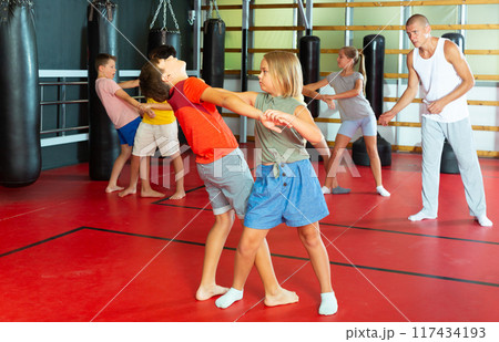 Preteen children practicing in pair self-defence movements with male trainer 117434193