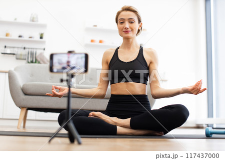 Woman practicing yoga at home while recording video for online class 117437000
