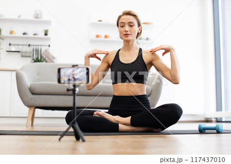 Woman practicing yoga at home recording fitness video Woman practicing yoga at home recording fitness video 117437010