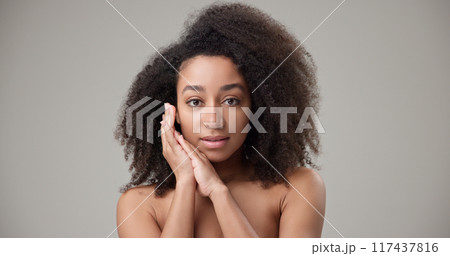 Beauty and Healthcare concept - Beautiful African American woman with curly afro hairstyle hair and clean, healthy skin on gray studio background posing and looking at camera Beauty and Healthcare concept - Beautiful African American woman with curly afro hairstyle hair and clean, healthy skin on gray studio background posing and looking at camera 117437816