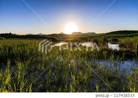 2024年夏曽爾高原お亀池の夕景　遠景の山並みへ沈んで行く太陽① 117438533
