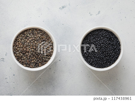Bowls with dry raw black and green lentils seeds on kitchen table. 117438961