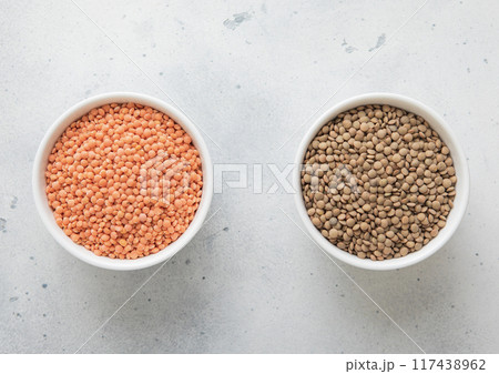Ceramic bowls with raw dry orange and white lentils seeds on kitchen table.Macro. 117438962