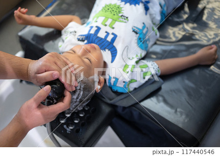 Child getting hair washed at a salon with a dinosaur-themed outfit on 117440546