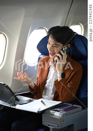 Modern young businessman wearing a brown jacket talking on mobile phone during a flight. Business travel concept Modern young businessman wearing a brown jacket talking on mobile phone during a flight. Business travel concept 117441348