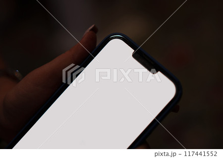 close-up. Smartphone with white screen in female hand on dark background.  117441552