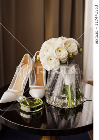 Bridal bouquet, white heeled shoes and a bottle of perfume on a black table. Bridal bouquet, white heeled shoes and a bottle of perfume on a black table. 117441553