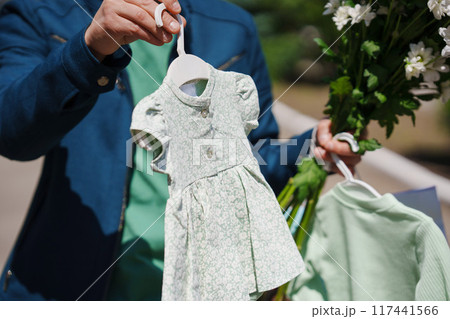 A man holds a small children's dress and a bouquet of flowers. 117441566