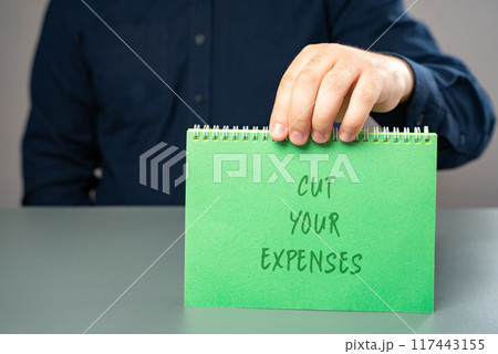 Notes Cut your expenses. Money management and budget planning. A man holds a note in his hands with an inscription. Notes Cut your expenses. Money management and budget planning. A man holds a note in his hands with an inscription. 117443155
