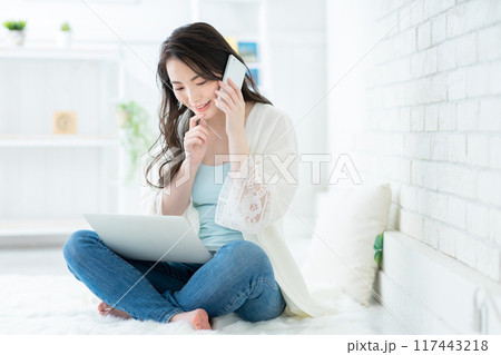 リビングでパソコンを見て電話をする若い女性 リビングでパソコンを見て電話をする若い女性 117443218