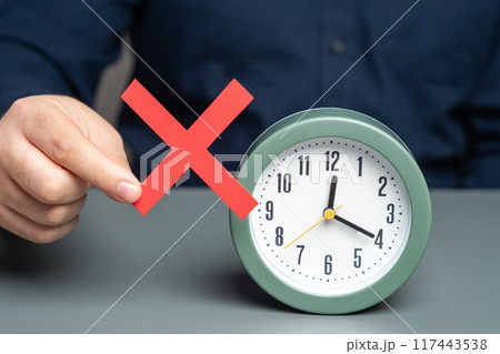 A man is holding a red no prohibition sign near clock. Prohibition of time change. Summer and winter time. Review laws, regulations 117443538