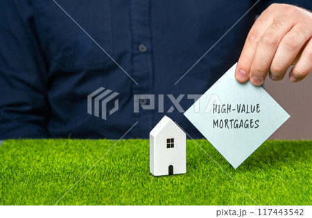 High-value mortgages concept. Loans provided for purchasing luxury or high-cost properties. Real estate and finance. A note in male hands and a miniature house 117443542