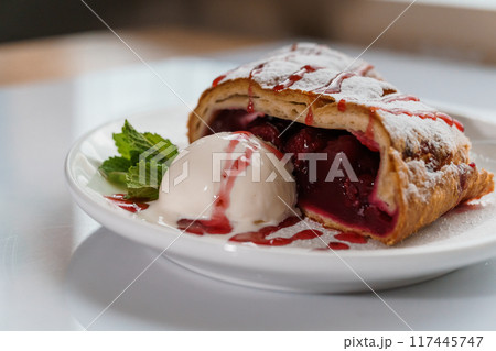 Dessert strudel with cherry and ice cream on a white plate 117445747