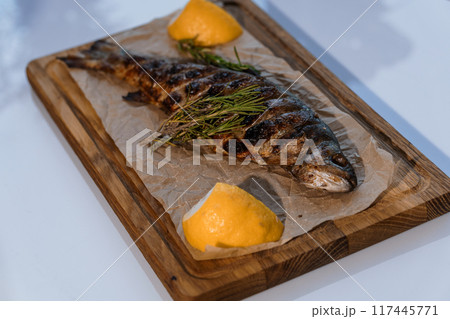 Dorado fish baked with lemon on a barbecue on a wooden board Dorado fish baked with lemon on a barbecue on a wooden board 117445771