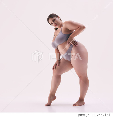 Full length photo of plus-size woman in underwear, showcasing her natural beauty and strength against white studio background. Full length photo of plus-size woman in underwear, showcasing her natural beauty and strength against white studio background. 117447121