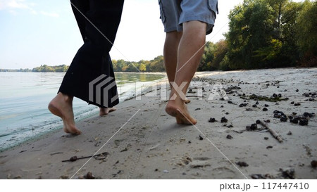 Bare feet of couple stepping together along beach at ocean background. Male and female legs of pair walking near sea. Happy lovers going on sandy shore. Concept of summer vacation or holiday. 117447410