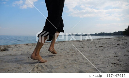 Bare feet of adult woman jogging on sand at the beach with seascape at background. Female legs running along sea shore. Happy lady spending time near ocean coast. Concept of summer vacation 117447413