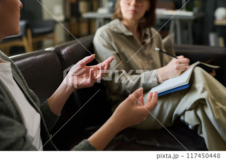 Two individuals engaging in counseling session on couch, one holding clipboard and pen, focusing on discussion, expressing thoughts with hand gestures Two individuals engaging in counseling session on couch, one holding clipboard and pen, focusing on discussion, expressing thoughts with hand gestures 117450448