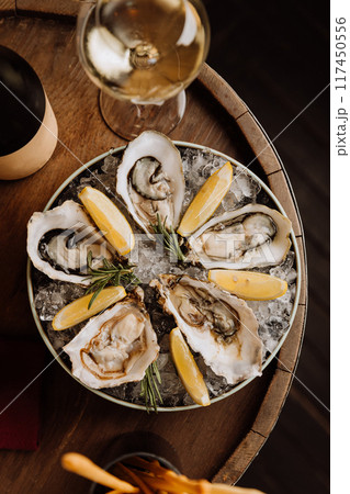 Fresh oysters on ice with lemon wedges and white wine, ideal for gourmet dining and celebrations Fresh oysters on ice with lemon wedges and white wine, ideal for gourmet dining and celebrations 117450556