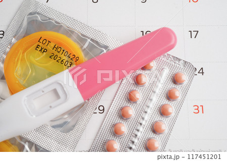 Pregnancy test with birth control pills and condom for female on calendar, ovulation day. 117451201